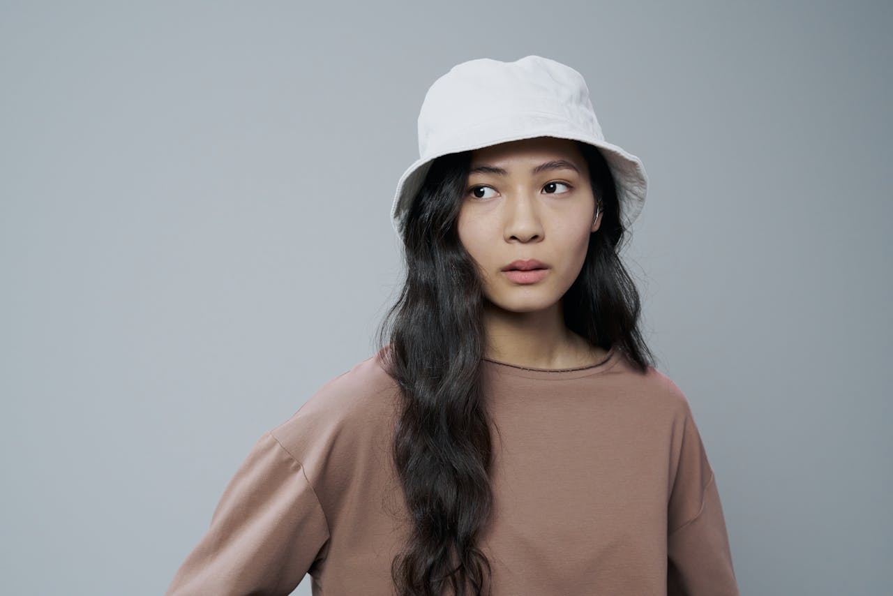 Studio portrait of a woman wearing a white bucket hat and casual clothing, looking away.